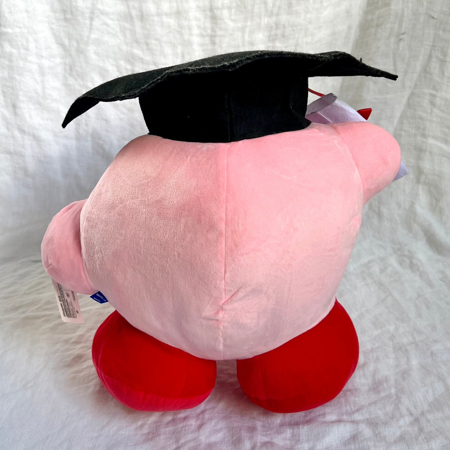 Back view of plush toy depicting the character Kirby, primarily in pink and red colors.