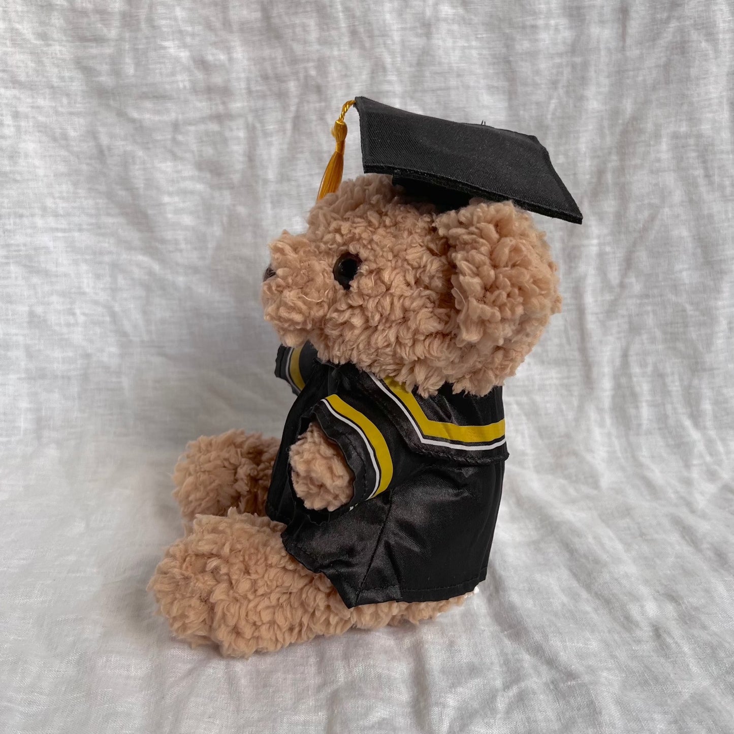 Front view of fluffy brown bear with graduation cap and gown containing yellow tassles and stripes