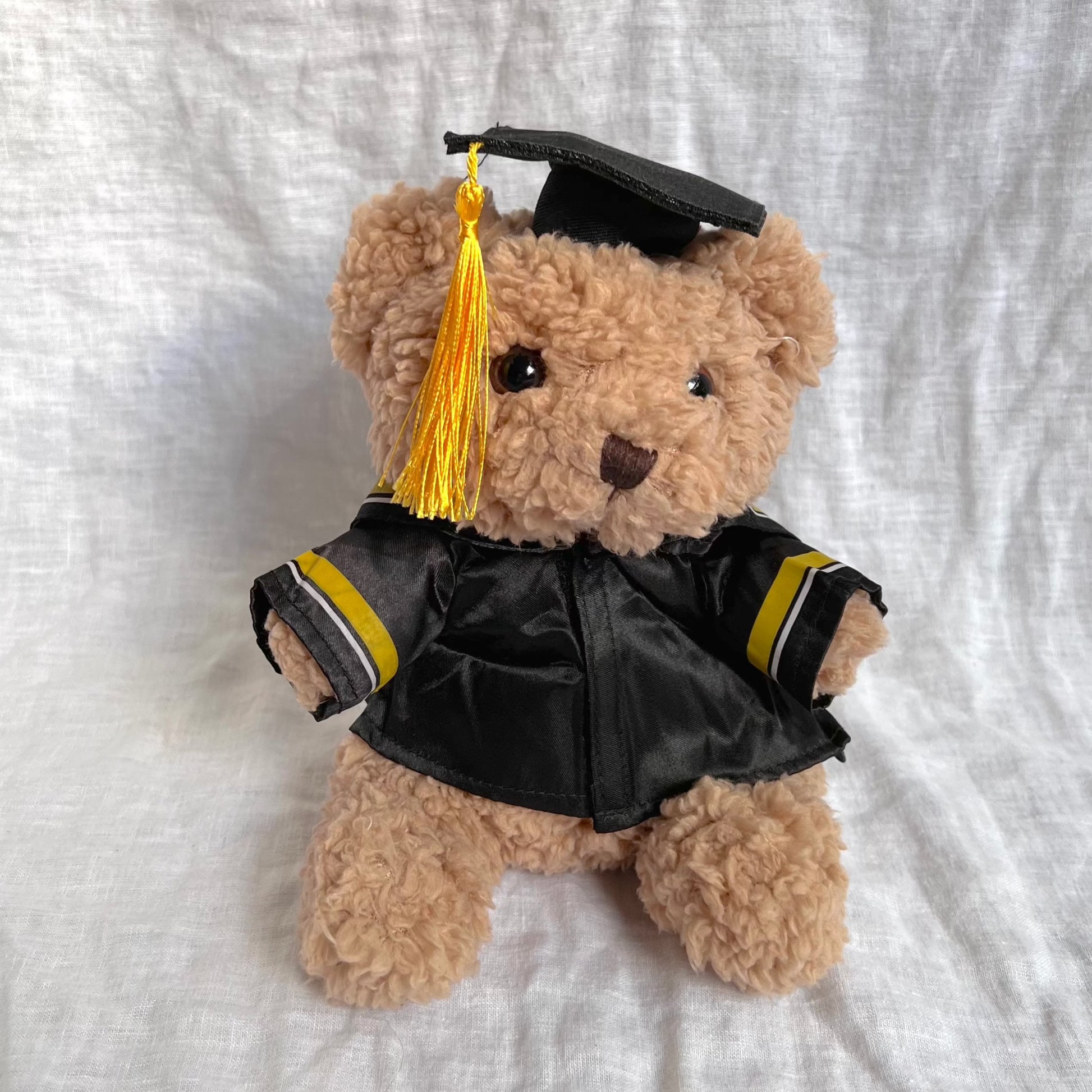 Front view of fluffy brown bear with graduation cap and gown containing yellow tassles and stripes