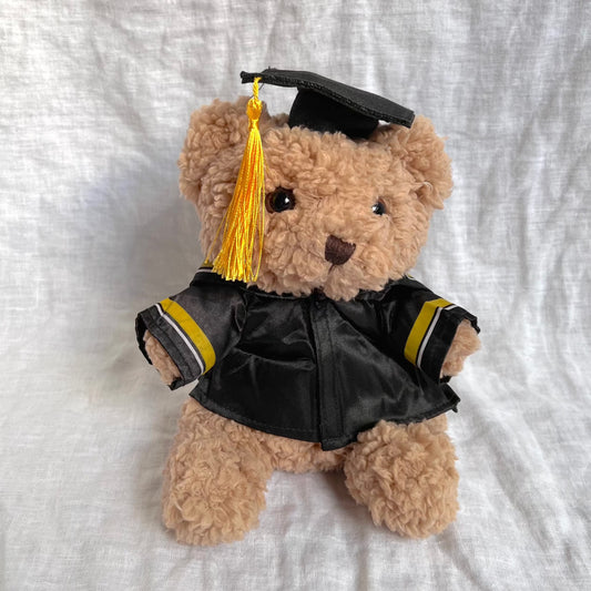 Front view of fluffy brown bear with graduation cap and gown containing yellow tassles and stripes